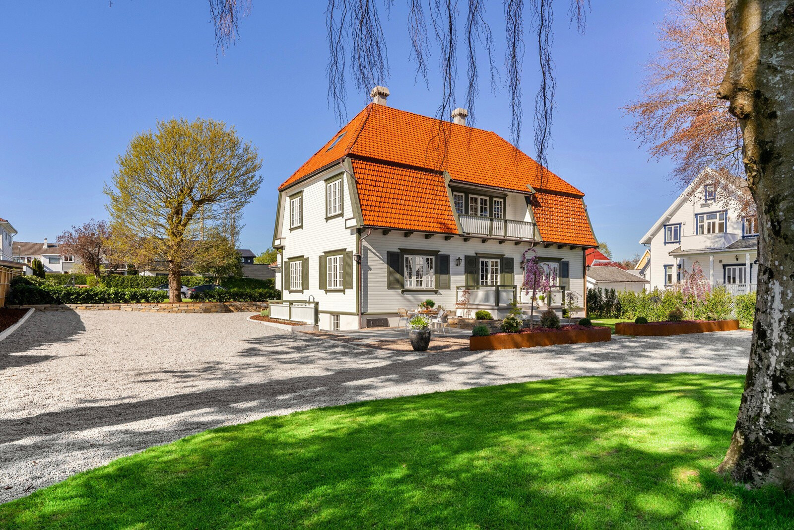 Villaens fasade sett over den runde plenen og den lyse grusgårdsplassen