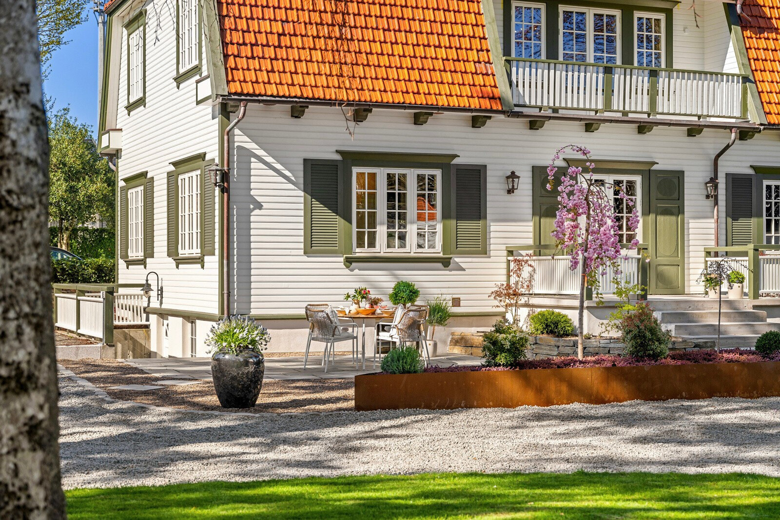 Terrasse ved fasaden med blomstrende klatreplante, cortenkant og grusdekke