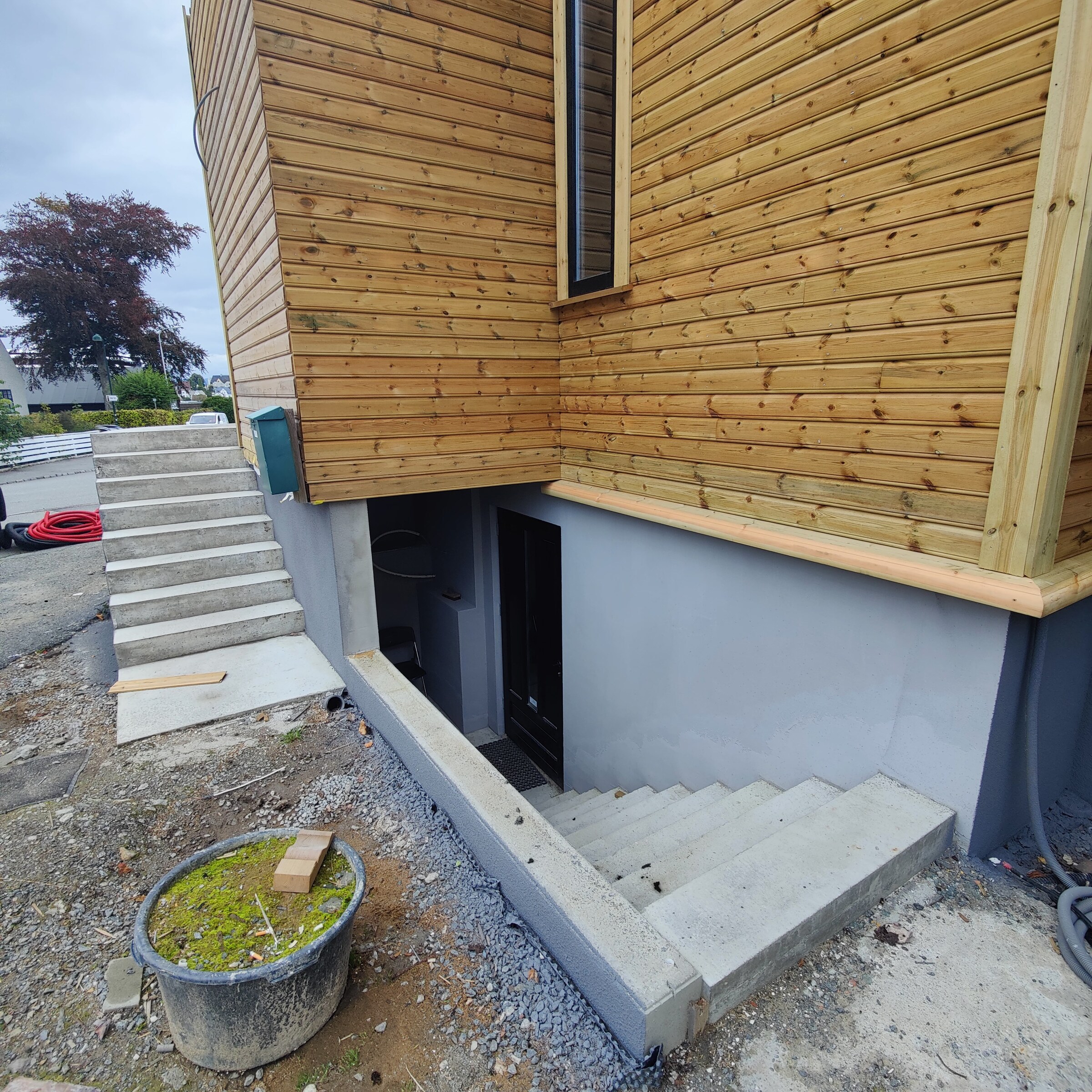 Ferdig kjellerinngang med betongtrapp, pusset støttemur og trekledd tilbygg