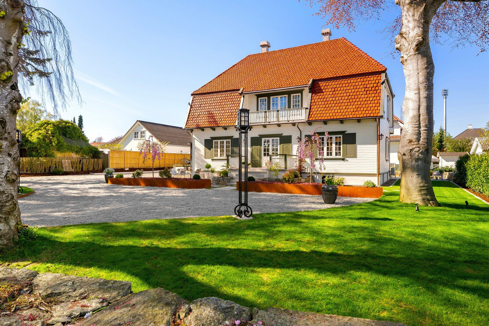 Villaen sett fra hagen med plen, hagelanterne og grusflate kantet med corten