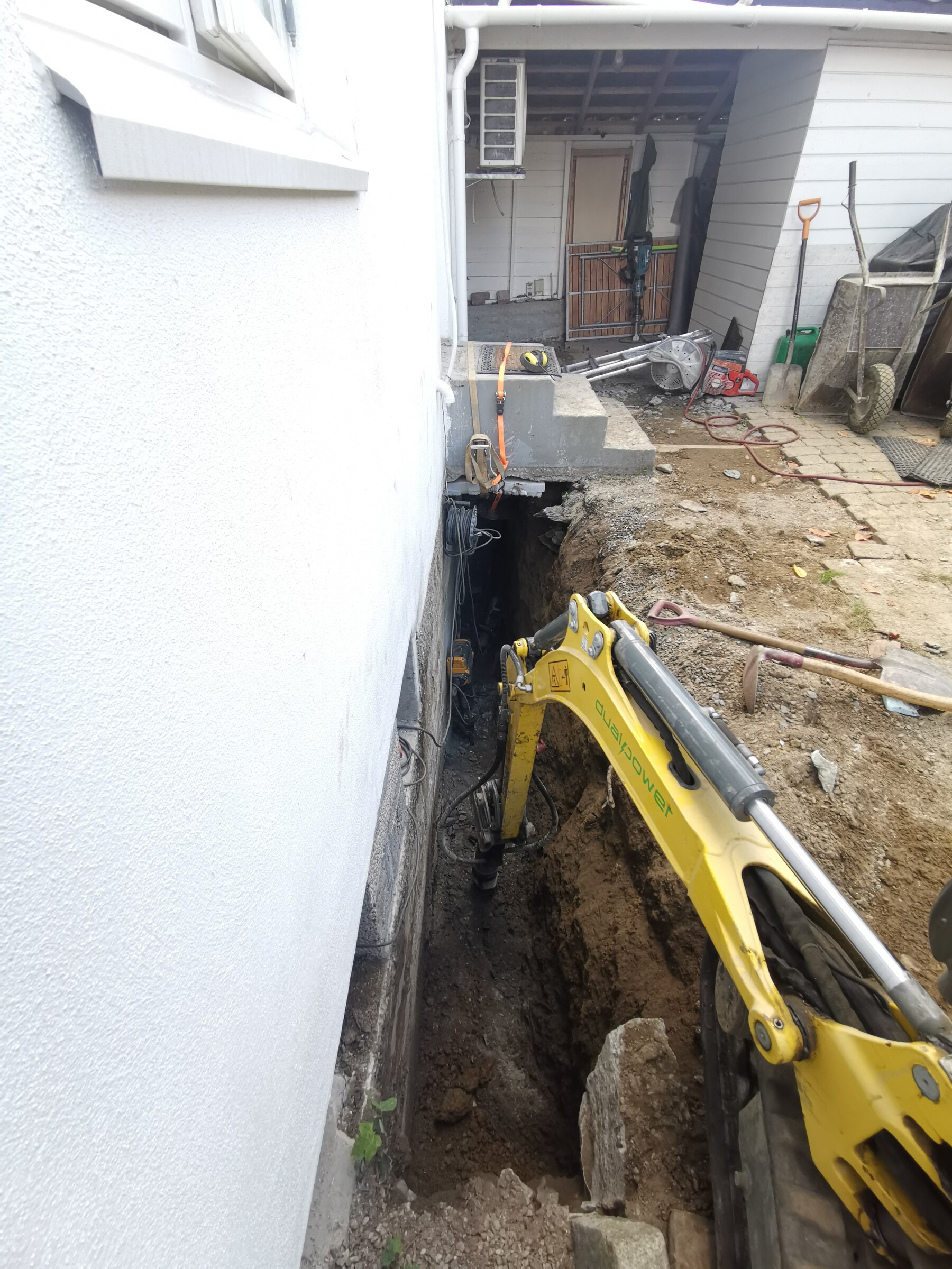 Gravemaskin i arbeid tett inntil fasaden