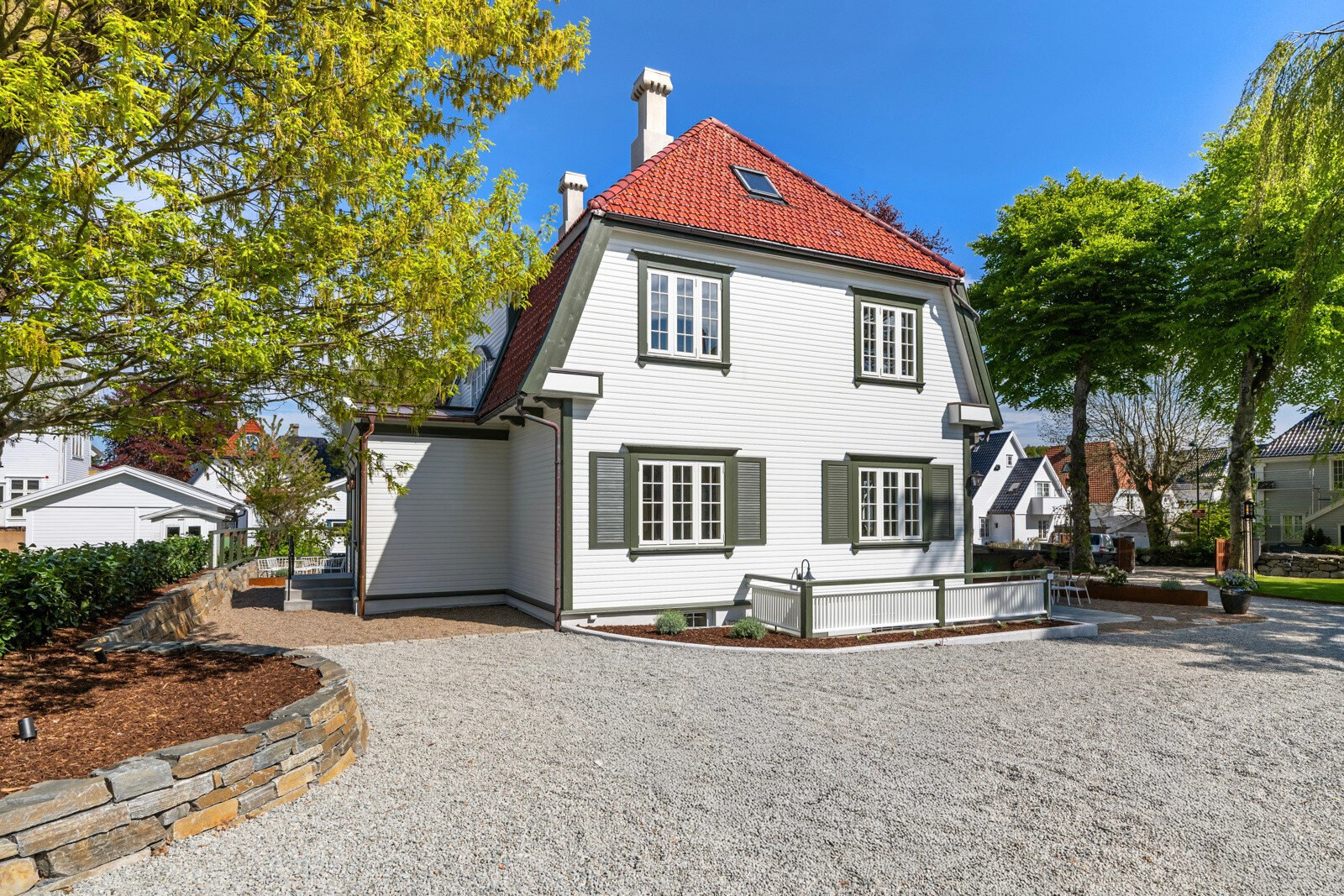 Hjørne av huset med natursteinsmur, barkbed og lys grusflate