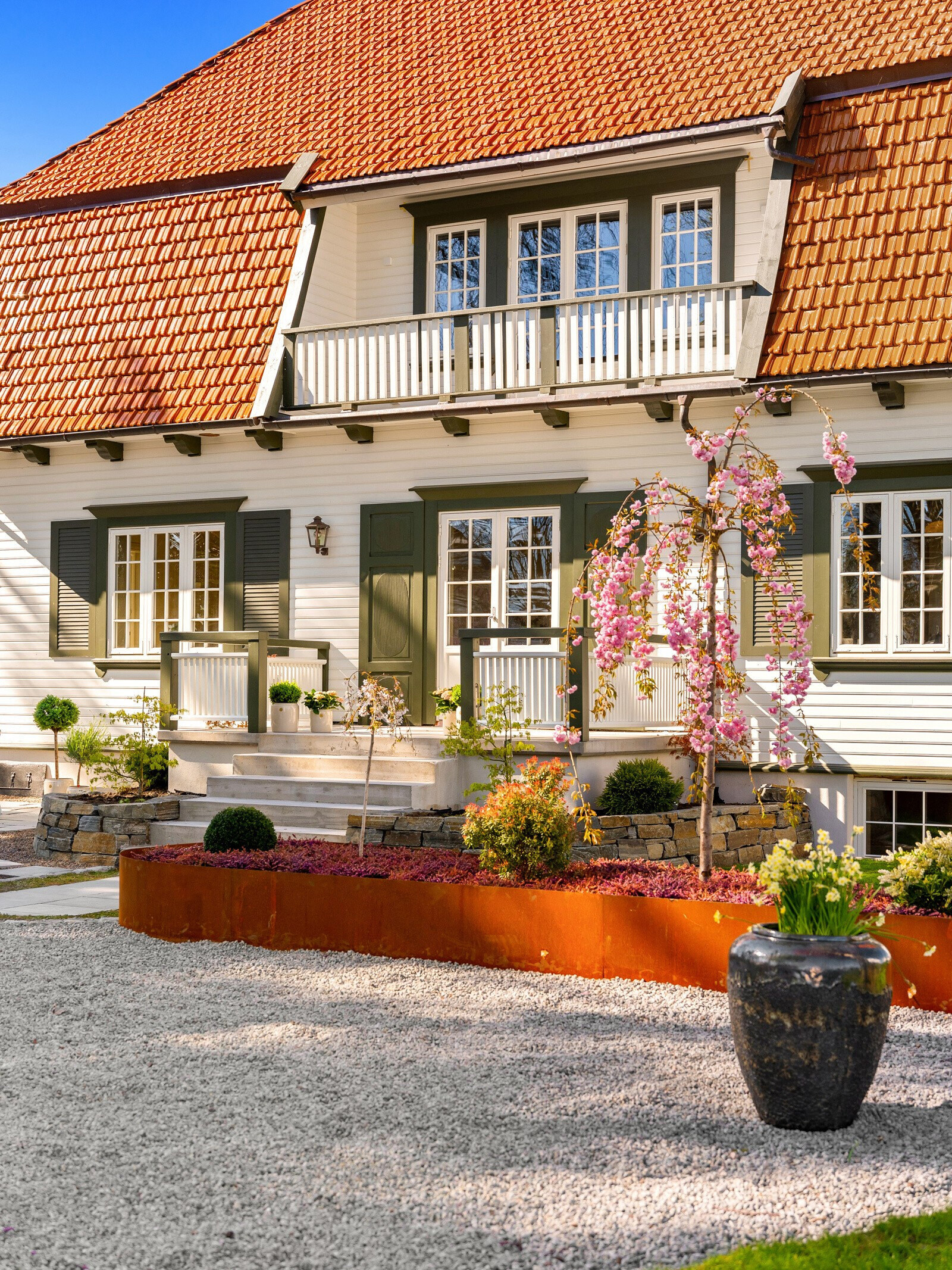Cortenplantekasse med beplantning og krukke foran inngangstrappen