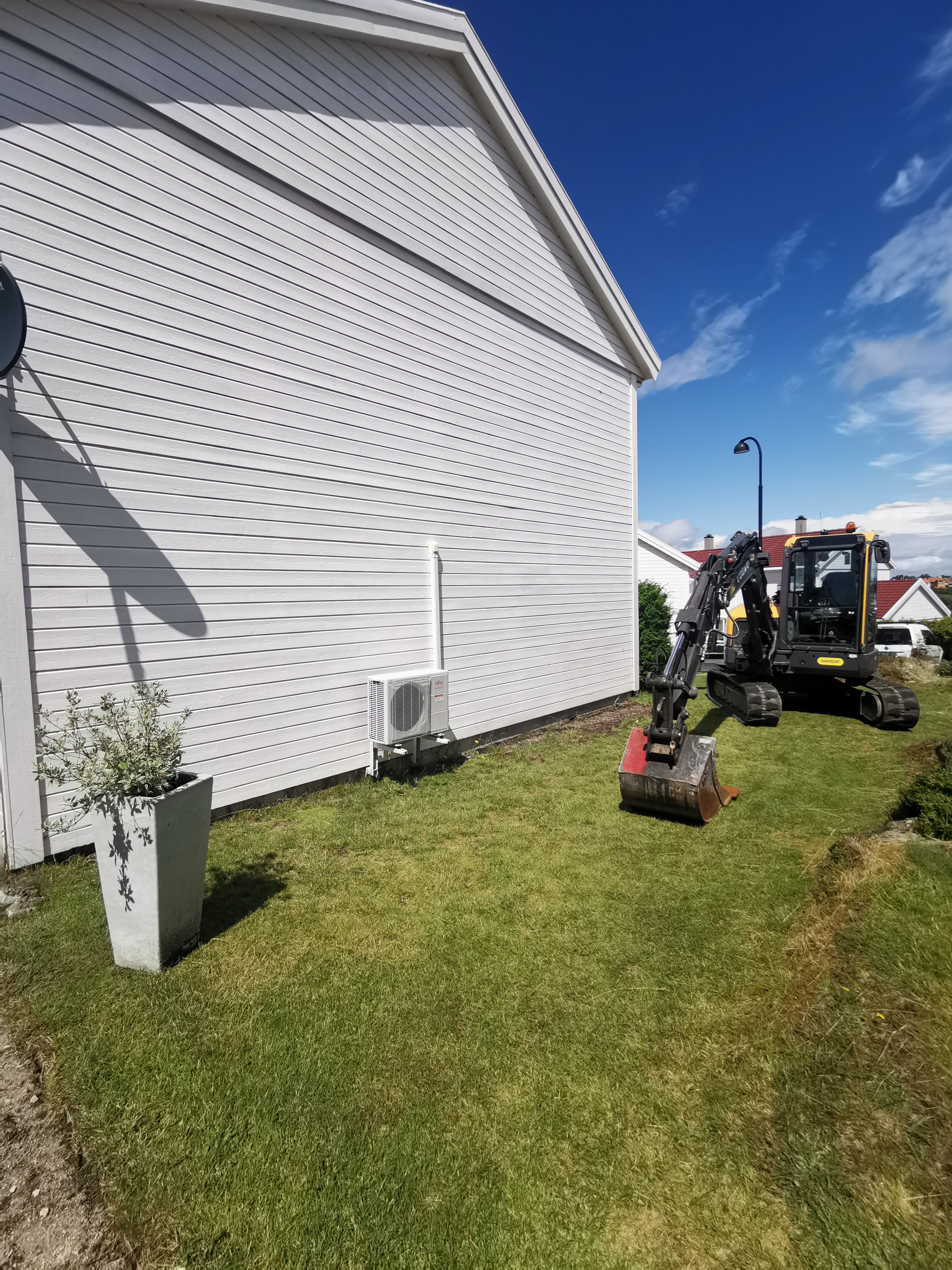 Gravemaskin i arbeid på plenen ved bygget