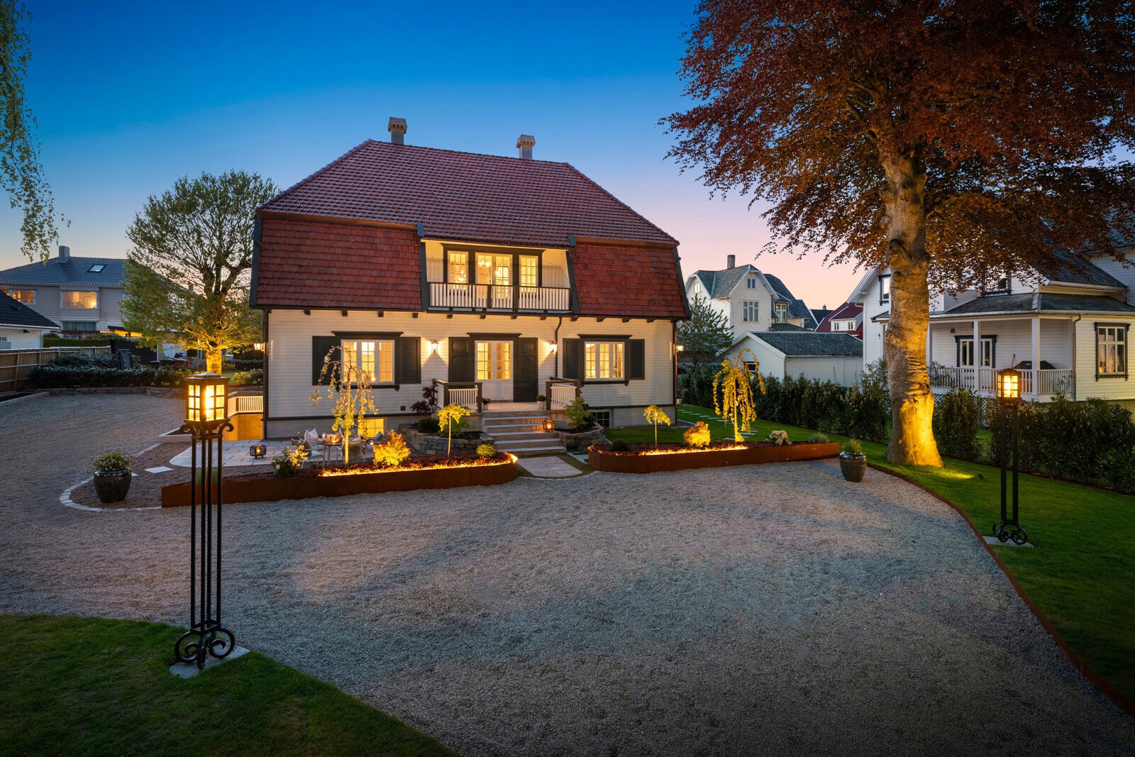 Villaen om kvelden med varm belysning, plantebed i corten og grusgårdsplass
